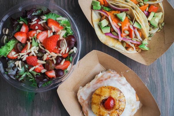 A fresh salad with strawberries, grapes, and sliced almonds, a glazed pastry with grilled pineapple, and tacos.
