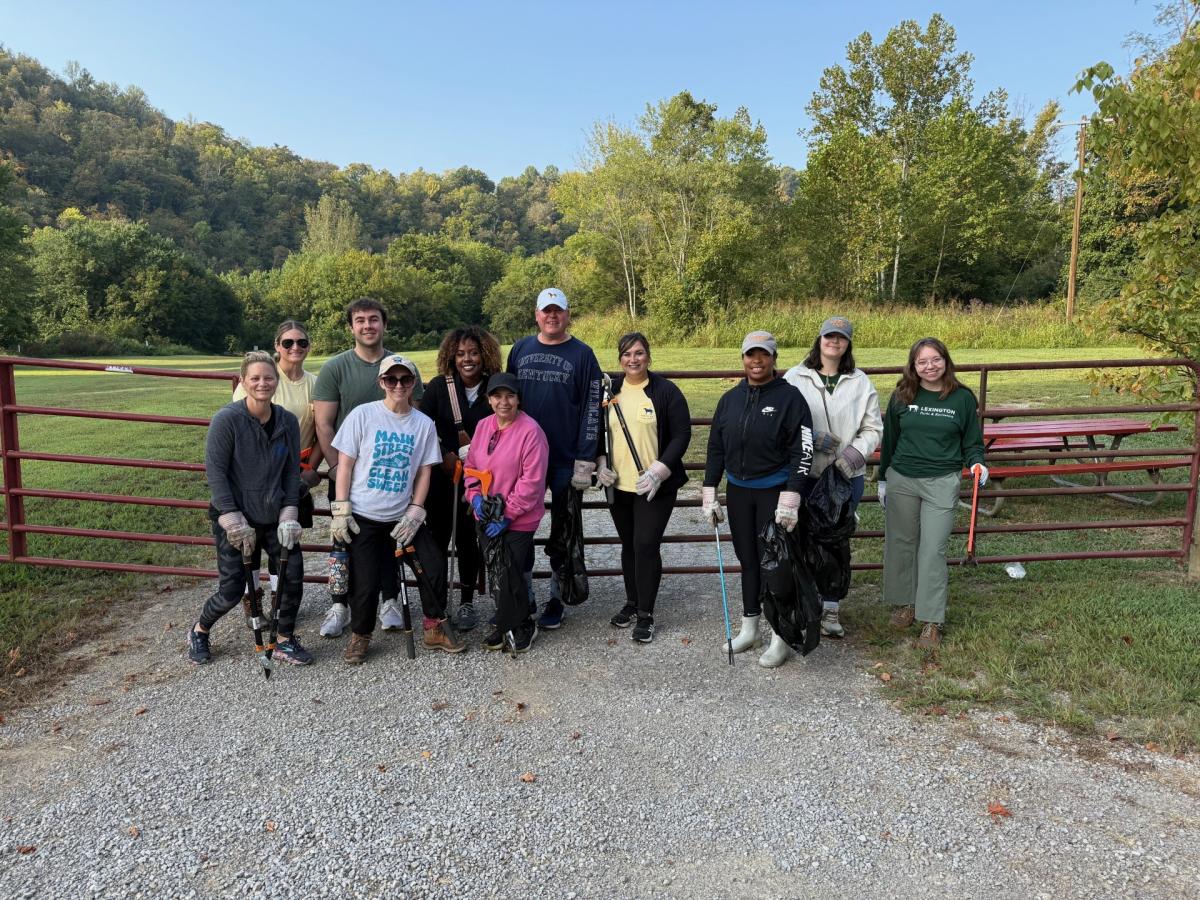 A group of people poses in front of a red metal fence with litter pickers