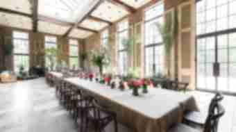 An elegant room that contains two long tables with small pink, green, and white bouquets arranged down the center of the table.