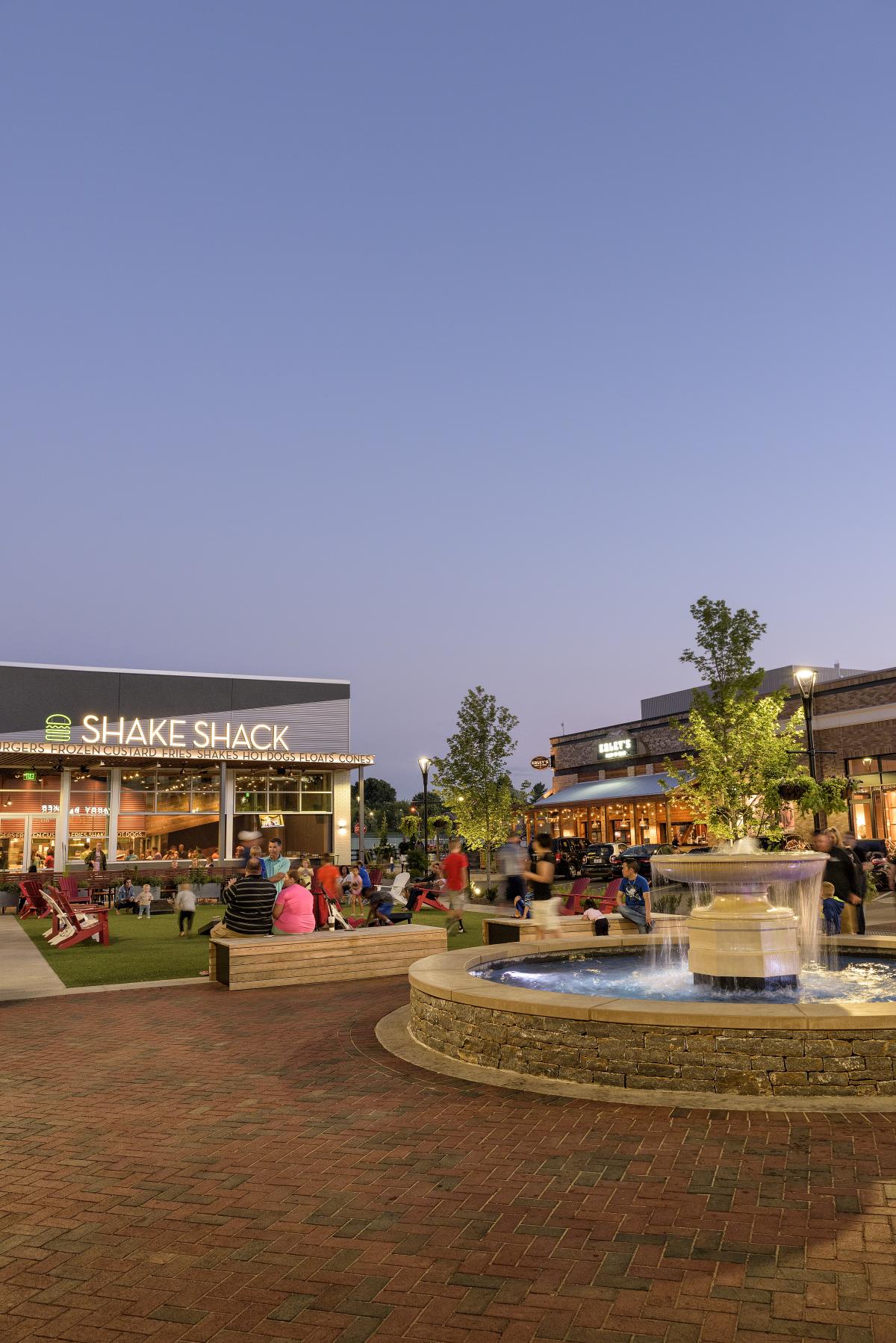 Court yard at a mall with a large fountain and plenty of people walking around the shops.